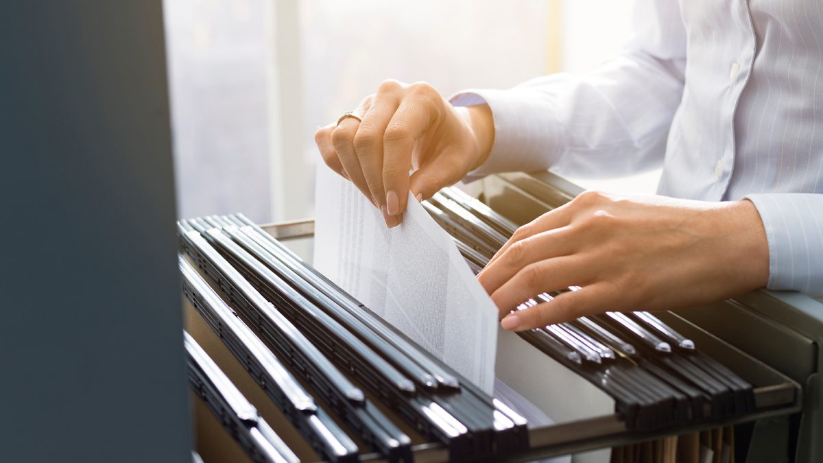 Professional female office clerk searching files and paperwork in the filing cabinet