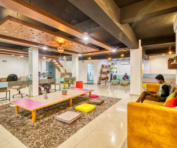 Visuel d'un open space d'une start up, longue table au milieu et une personne assise dans le canapé