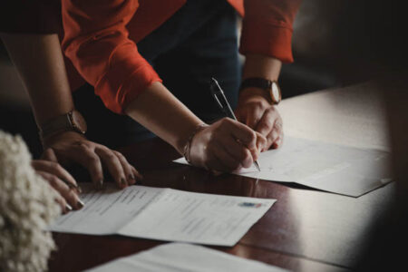 2 personnes dont une personne qui signe un document avec son crayon