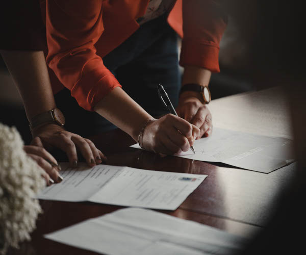 2 personnes dont une personne qui signe un document avec son crayon